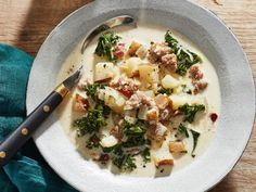 a white bowl filled with soup and potatoes on top of a wooden table next to a spoon