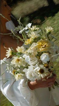 a woman holding a bouquet of white and yellow flowers in her hands while walking through the grass