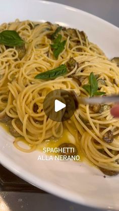 a plate of spaghetti with olives and spinach on it, being cut by a pair of scissors