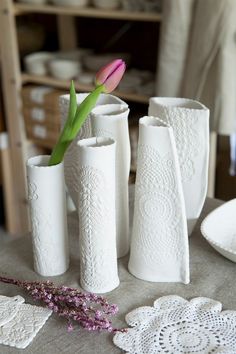 four white vases with pink flowers in them on a table cloth and doily