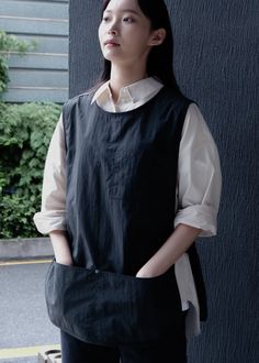 a woman standing next to a building with her hands in her pockets and looking off into the distance