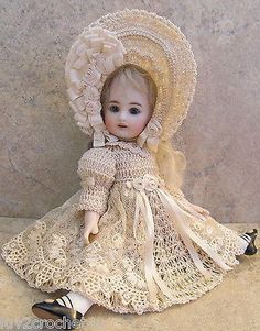 a doll is sitting on the ground wearing a dress and bonnet