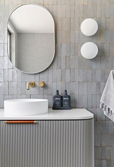 a white sink sitting under a round mirror next to a wall mounted faucet