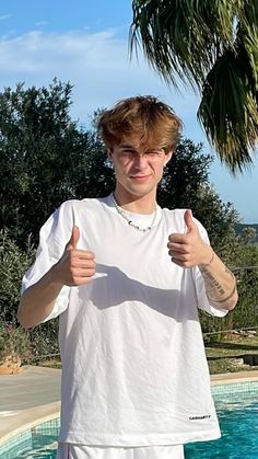 a young man standing next to a pool giving the thumbs up