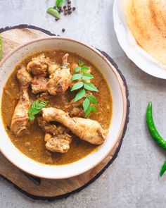 a white bowl filled with chicken curry next to green peppers