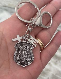 a hand holding a metal keychain with a cross and shield on the front