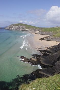 the beach is surrounded by rocky cliffs and clear blue water, with green hills in the background