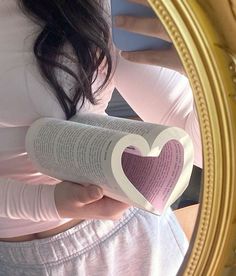 a woman reading a book in front of a mirror with a heart cut out on it