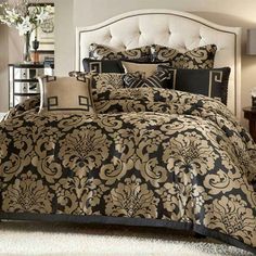 a bed with black and gold comforters in a bedroom next to a night stand