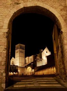 an archway leading to a building with a clock tower in the background at night time