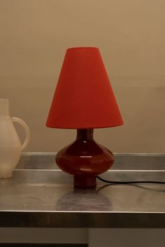 a red lamp sitting on top of a metal table next to a white vase and pitcher