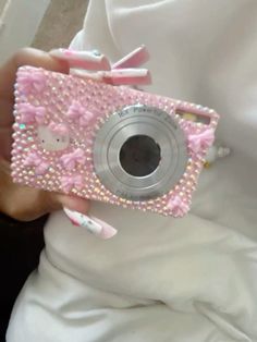 a person holding a camera in their hand with pink and white decorations on it's body