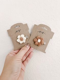 two small white and brown flower clip on top of each other in front of a paper bag