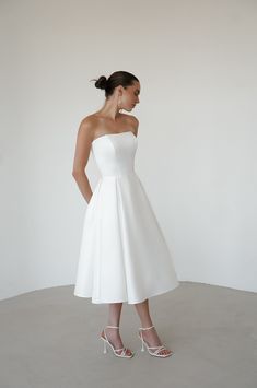 Elevate your wedding day look with our exquisite satin minimalist wedding dress. This sophisticated dress features a graceful midi length, perfect for the modern bride seeking timeless elegance. Discreet side pockets add a practical and stylish touch. A romantic lace-up back detail offers a customizable fit and a hint of classic charm. Crafted from luxurious satin, this dress combines simplicity with refined beauty, making it an ideal choice for your special day. Rehearsal Dinner Dress For Bride Elegant, Wedding Dress Low Heels, Wedding Dresses Medium Length, Reception Dress Short Bride, Classy White Midi Dress, Bridal Midi Dress, Second Look Wedding Dress Short, Ankle Wedding Dress, Simple Civil Wedding Dress Courts