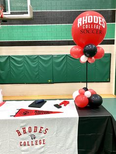 a table with some balloons on it in front of a basketball court and green wall