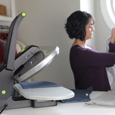 a woman sitting at a desk with a laptop computer on top of it and an ironing board in front of her