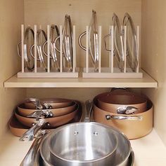 pots and pans are lined up on shelves in a cupboard with utensils