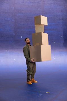 a man holding a stack of boxes on top of his head while standing in front of a blue background