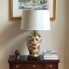 a lamp sitting on top of a wooden table next to a painting and a book