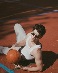 a man sitting on the ground with a basketball in his hand and sunglasses on top of his head