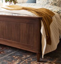 a bed with a blanket on top of it next to a rug and window sill