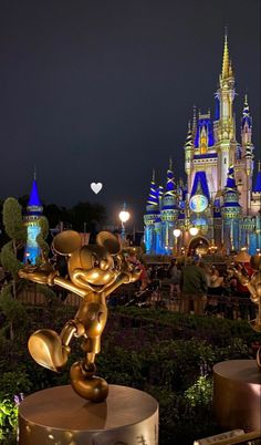 mickey mouse statue in front of the castle at night