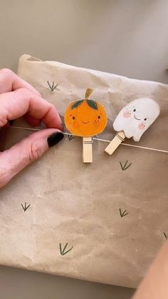 a person is holding a piece of paper with some stick decorations on it and two small pumpkins