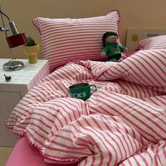 a bed with pink and white striped comforter next to a night stand on the floor