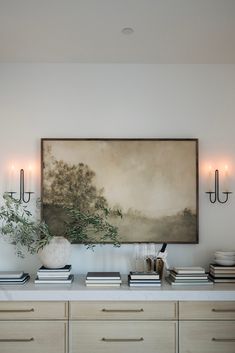 a painting is hanging on the wall above a dresser with books, candles and vases