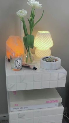 two white flowers sitting on top of each other next to a lamp and some books