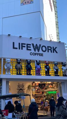 people walking in front of a coffee shop with fake bears on the display window and sign that says life work coffee