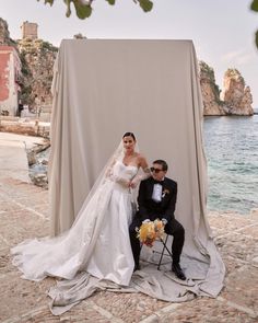 a bride and groom pose for a photo in front of an outdoor backdrop with the ocean behind them