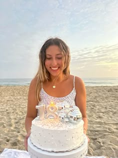 a woman sitting in front of a white cake on top of a beach