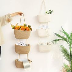 a woman is standing next to a wall with three baskets hanging from it's sides