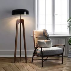 a chair sitting next to a lamp on top of a hard wood floor in front of a window