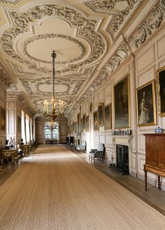 an ornately decorated hallway with chandeliers and paintings on the walls, along with two fireplaces