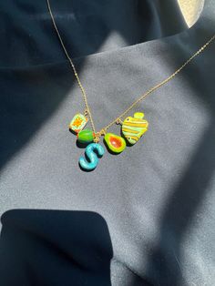 three colorful necklaces hanging from a gold plated chain on a black cloth background