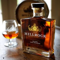 a bottle of liquor sitting on top of a wooden table next to a glass filled with liquid