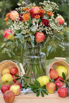 A floral arrangement adorned with mums, eucalyptus, and apples along with bushel baskets overflowing with apples create the perfect centerpiece for an Apple Harvest Tablescape. Apple Display Table, Pumpkins And Apples Decor, Fall Apple Party Decorations, Apple Harvest Party Ideas, Apple Festival Decorations, Apple Boquet, Red Apple Centerpiece Ideas, Apple Floral Arrangement, Fall Event Theme Ideas