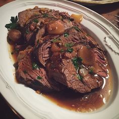 a white plate topped with meat and vegetables covered in gravy on top of a wooden table