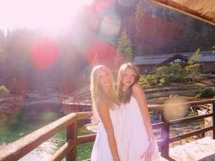 two girls are standing on a deck near the water