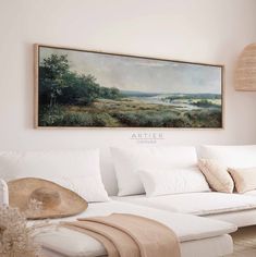 a painting hanging on the wall above a white couch with pillows and throw pillows in front of it