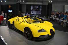 a yellow bugatti is on display at a car show with people looking around