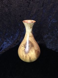 a small wooden vase sitting on top of a black cloth covered tablecloth with a light shining in it's center