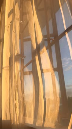 the sun is shining through sheer curtains in front of a window with blue sky and clouds