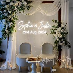 two chairs sitting in front of a white backdrop with flowers and greenery on it