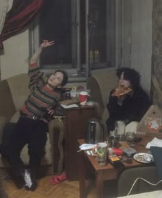 two people sitting on couches in a living room with one holding up his hand