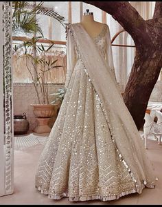 a white and gold lehenga with sequins on the skirt is displayed in front of a tree