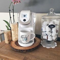 a coffee maker sitting on top of a wooden table next to a vase filled with flowers