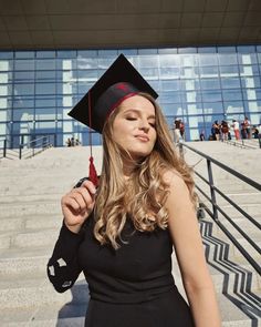 a young woman wearing a graduation cap and gown holding a red object in her hand